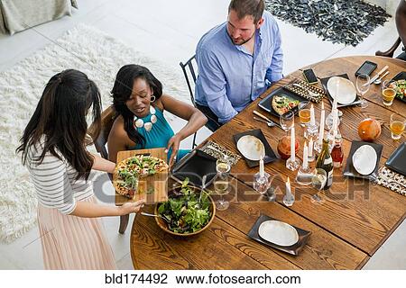 Stock Image - Woman serving friends at dinner party. Fotosearch