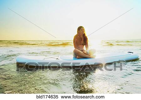 Stock Photography - Woman sitting on paddleboard in lake. Fotosearch