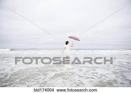 Woman wading with umbrella on beach View Large Photo Image Picture - Woman wading with umbrella on beach. Fotosearch
