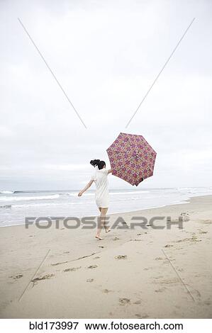Woman walking in wind with umbrella on beach View Large Photo Image Stock Photo - Woman walking in wind with umbrella on beach. Fotosearch