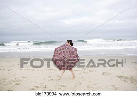 Picture - Woman walking with umbrella on beach. Fotosearch