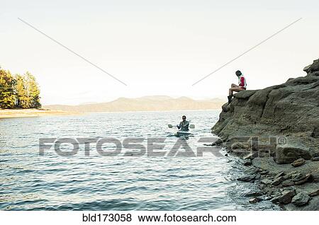 Stock Photo - Woman watching boyfriend rowing kayak in lake. Fotosearch