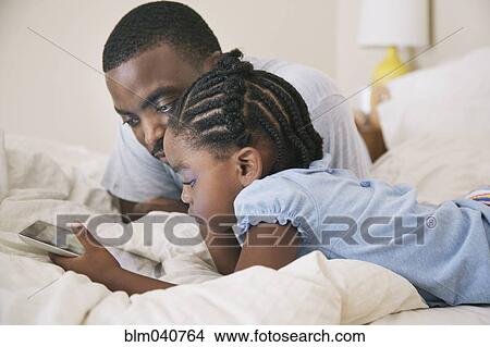 African American father and daughter using digital tablet on bed View Large Photo Image Picture - African American father and daughter using digital tablet on bed. Fotosearch