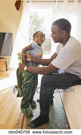 Stock Photo - African American father helping daughter put on costume. Fotosearch