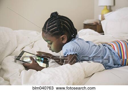 Stock Image - African American girl using digital tablet on bed. Fotosearch