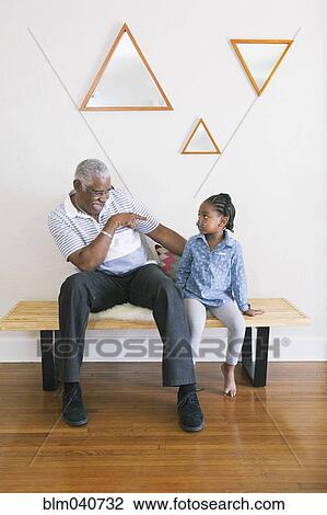 Stock Image - African American grandfather pointing at granddaughter on bench. Fotosearch