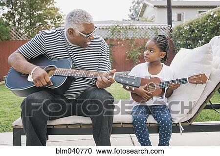 Stock Image - African American grandfather teaching granddaughter to play guitar. Fotosearch