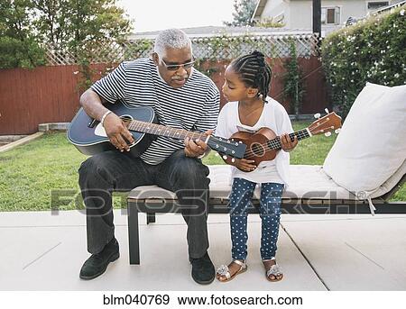 Stock Photo - African American grandfather teaching granddaughter to play guitar. Fotosearch