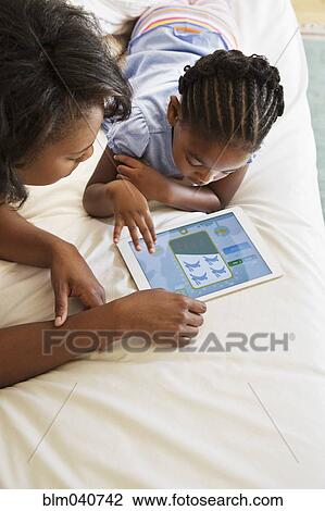 Stock Image - African American mother and daughter using digital tablet. Fotosearch