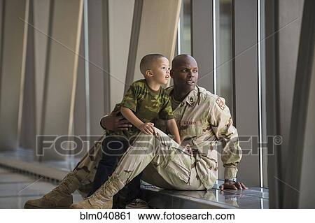 Stock Image - African American soldier and son looking out airport window. Fotosearch