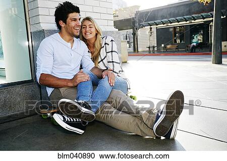 Stock Image - Caucasian couple sitting on sidewalk. Fotosearch