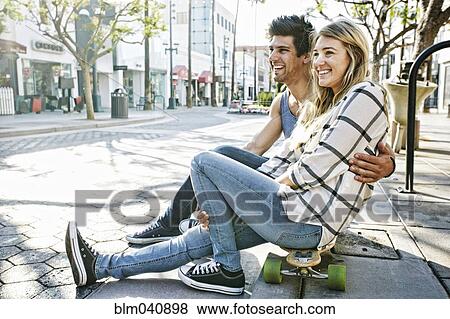 Stock Photo - Caucasian couple sitting on skateboards. Fotosearch
