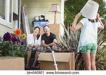Stock Image - Caucasian parents watching daughter play outside house. Fotosearch