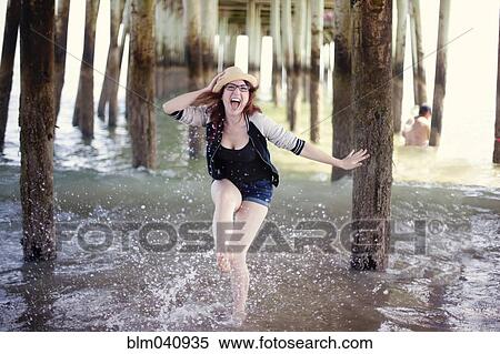 Stock Photography - Caucasian woman splashing in ocean under boardwalk. Fotosearch