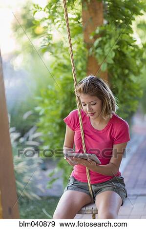 Stock Photo - Mixed race woman using digital tablet on swing. Fotosearch