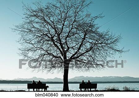 Stock Image - People sitting on benches at lake. Fotosearch