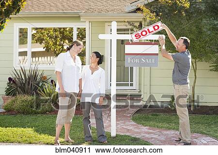 Stock Image - Real estate agent hanging sign outside house. Fotosearch
