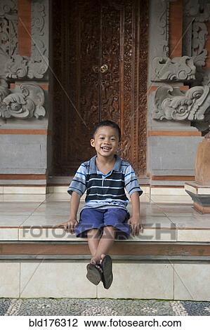 Stock Image - Asian boy sitting outside ornate building. Fotosearch