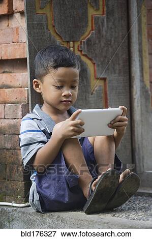 Stock Photo - Asian boy using cell phone on front step. Fotosearch