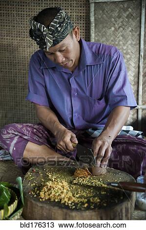 Stock Image - Asian man grinding spices on cutting board. Fotosearch