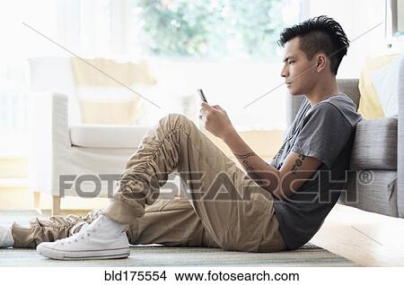 Asian man using cell phone in living room View Large Photo Image Picture - Asian man using cell phone in living room. Fotosearch
