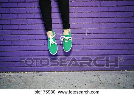 Stock Image - Asian woman jumping near brick wall. Fotosearch