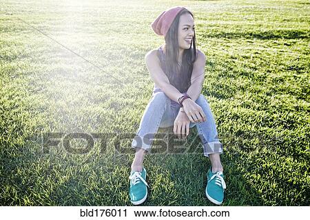 Stock Image - Asian woman sitting in grass. Fotosearch