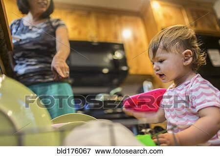 Stock Photo - Baby girl helping mother load dishwasher. Fotosearch