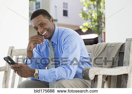 Stock Photo - Black businessman using cell phone on bench. Fotosearch