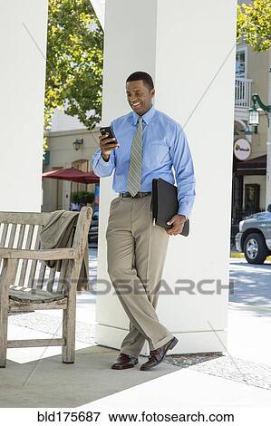 Stock Photo - Black businessman using cell phone outdoors. Fotosearch
