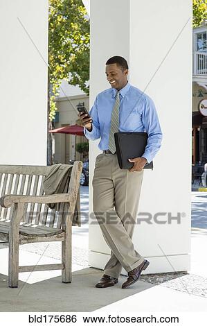 Stock Photograph - Black businessman using cell phone outdoors. Fotosearch