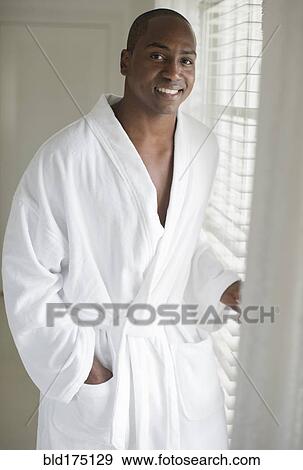 Stock Photo - Black man in bathrobe standing at window. Fotosearch