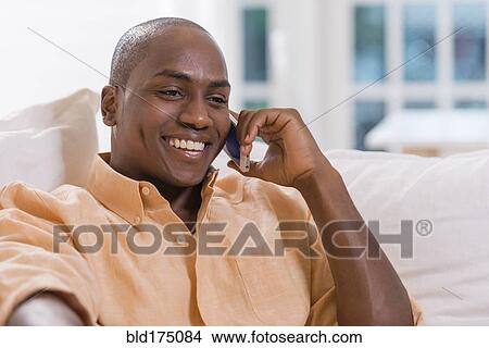 Black man talking on cell phone on sofa View Large Photo Image Picture - Black man talking on cell phone on sofa. Fotosearch