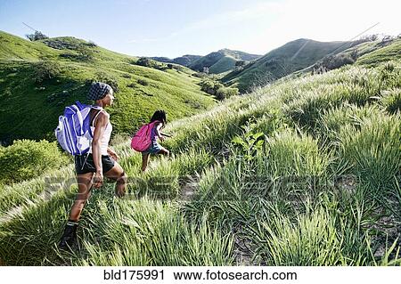 Stock Image - Black mother and daughter walking on rural hillside. Fotosearch