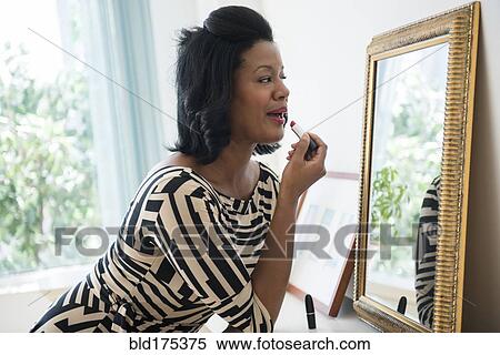 Stock Photography - Black woman applying lipstick in mirror. Fotosearch