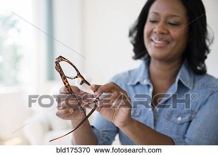 Stock Image - Black woman cleaning eyeglasses. Fotosearch