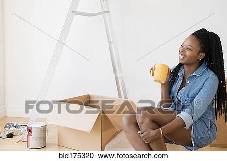 Stock Image - Black woman drinking coffee in new home. Fotosearch