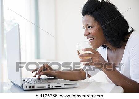 Stock Photograph - Black woman drinking wine and using laptop. Fotosearch