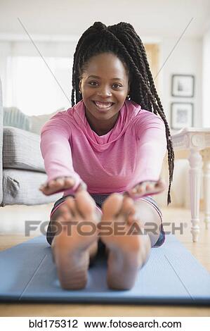 Stock Image - Black woman practicing yoga in living room. Fotosearch