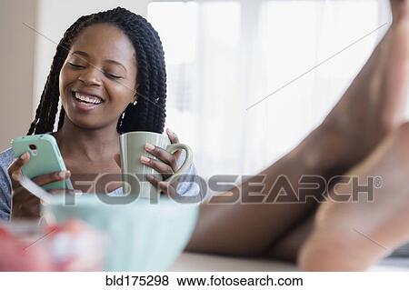 Stock Photo - Black woman using cell phone and drinking coffee. Fotosearch