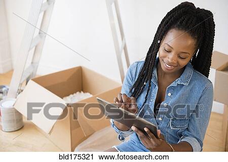 Stock Image - Black woman using digital tablet in new home. Fotosearch