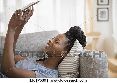 Stock Image - Black woman using digital tablet on sofa. Fotosearch
