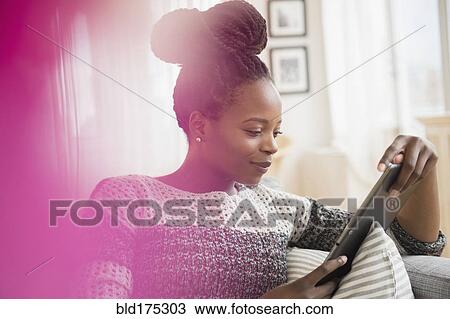 Stock Image - Black woman using digital tablet on sofa. Fotosearch