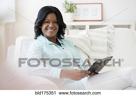 Stock Image - Black woman using digital tablet on sofa. Fotosearch