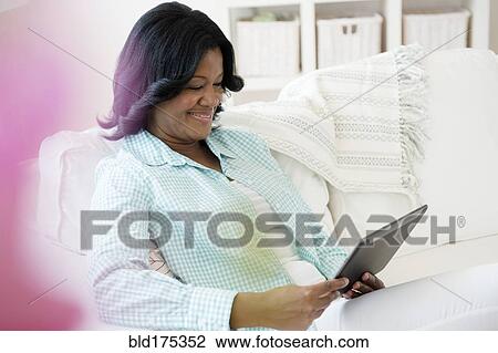 Stock Image - Black woman using digital tablet on sofa. Fotosearch