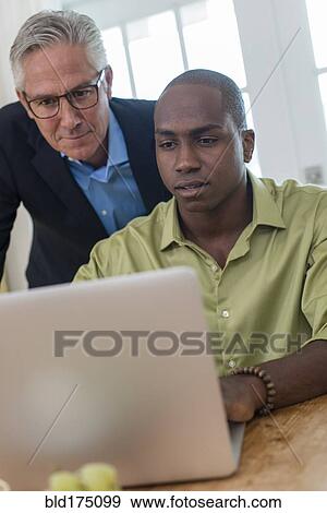 Stock Photo - Businessmen using laptop at desk. Fotosearch