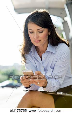 Stock Photography - Caucasian businesswoman using cell phone at bus stop. Fotosearch