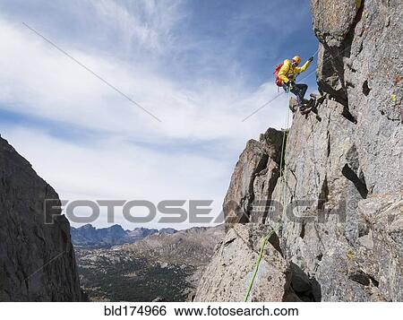 Stock Photograph - Caucasian climber rappelling on mountainside. Fotosearch
