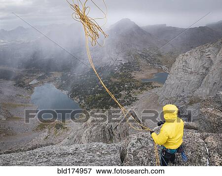 Stock Photo - Caucasian climber throwing rope down mountainside. Fotosearch