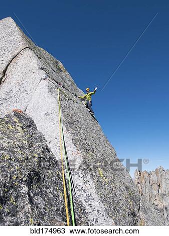 Stock Image - Caucasian climber waving on mountainside. Fotosearch
